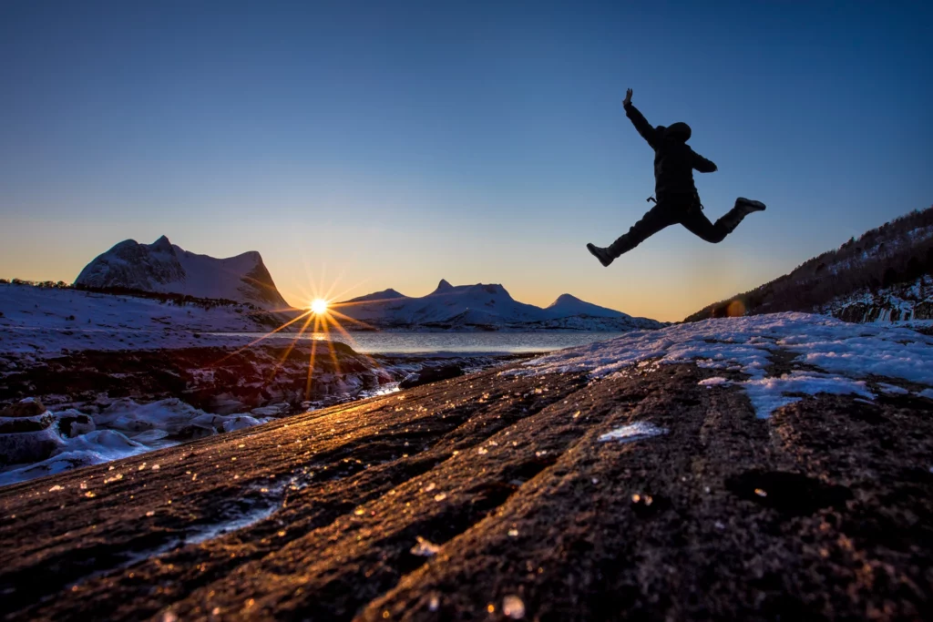 En person som hopper over et berg i solnedgangen.