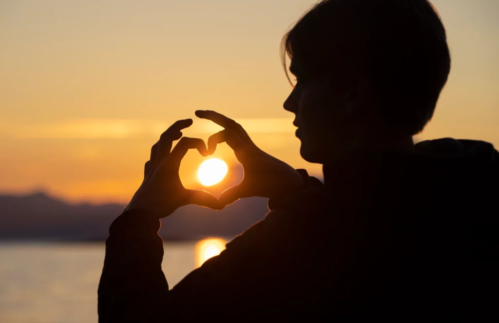 En mann som lager et hjerte med fingrene sine rundt sola.